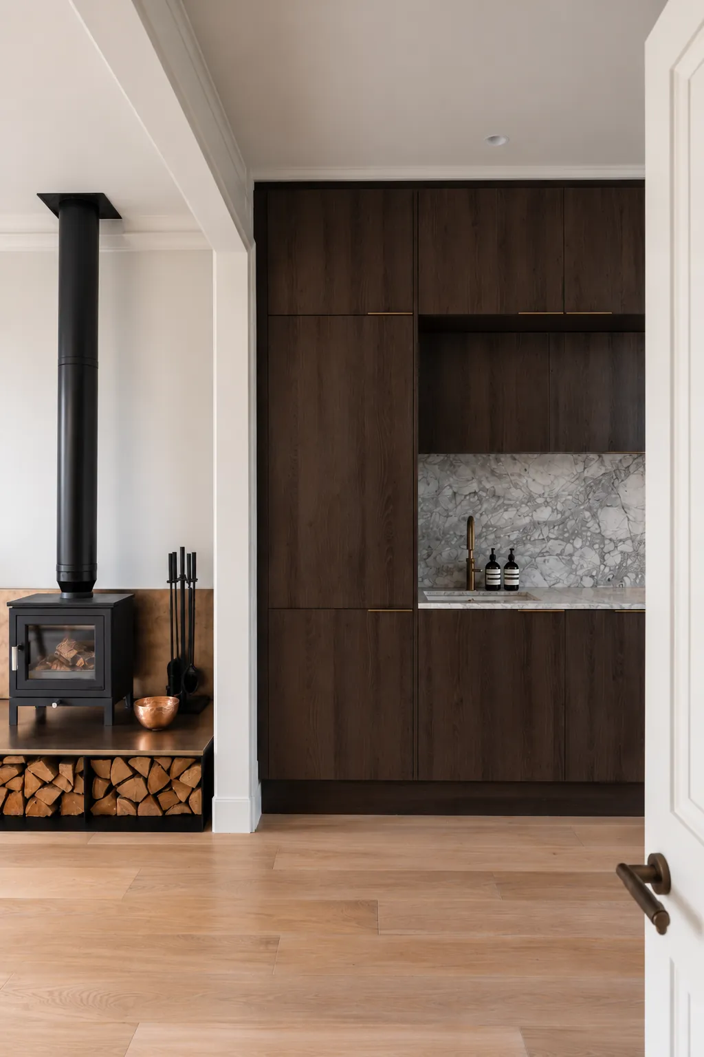 Log burner on a raised plinth with a log store, beside dark oak kitchen units and a marble splashback