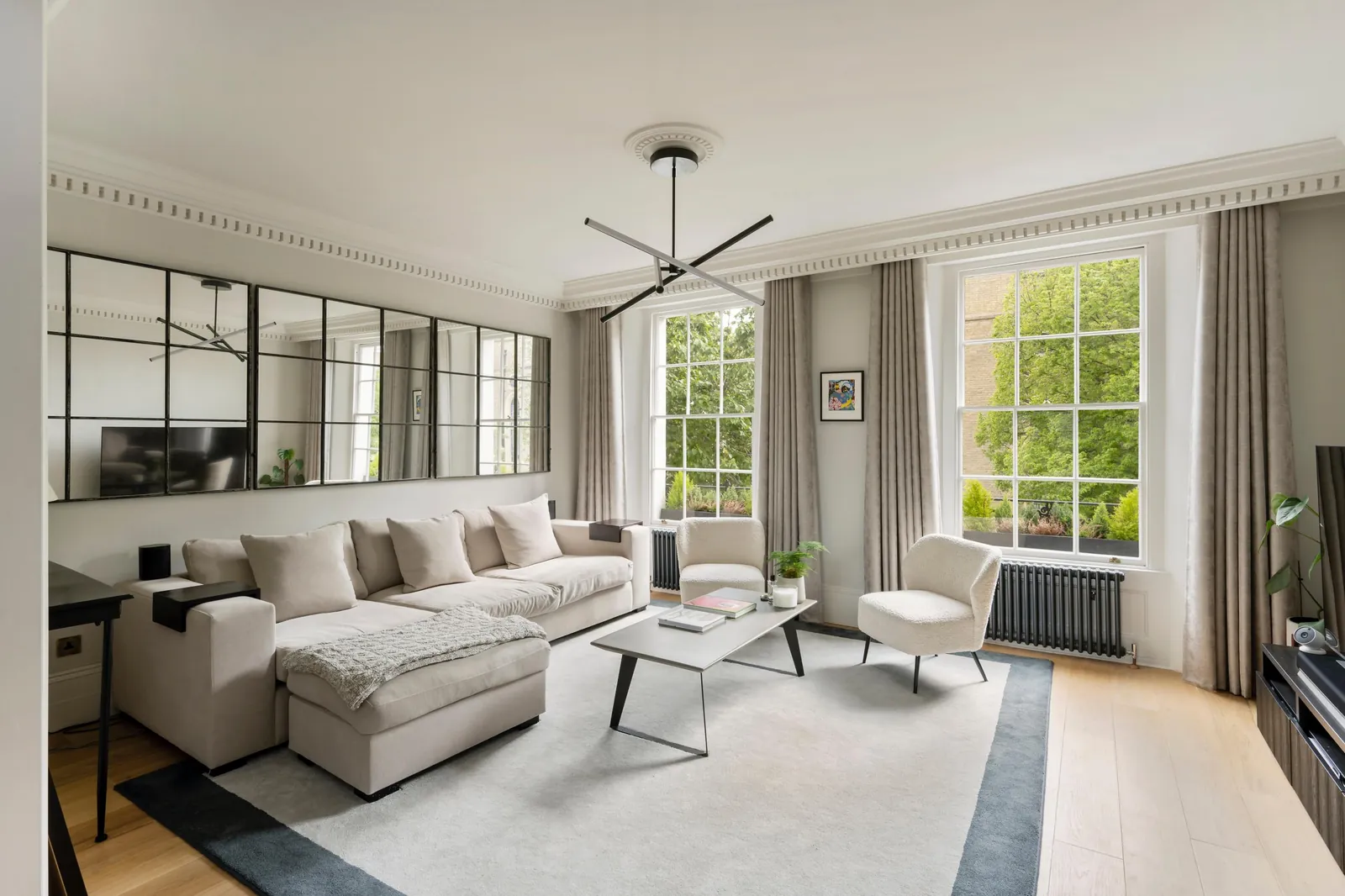 Living room with dentil cornicing, two tall sash windows, grid mirrors and a pale sofa