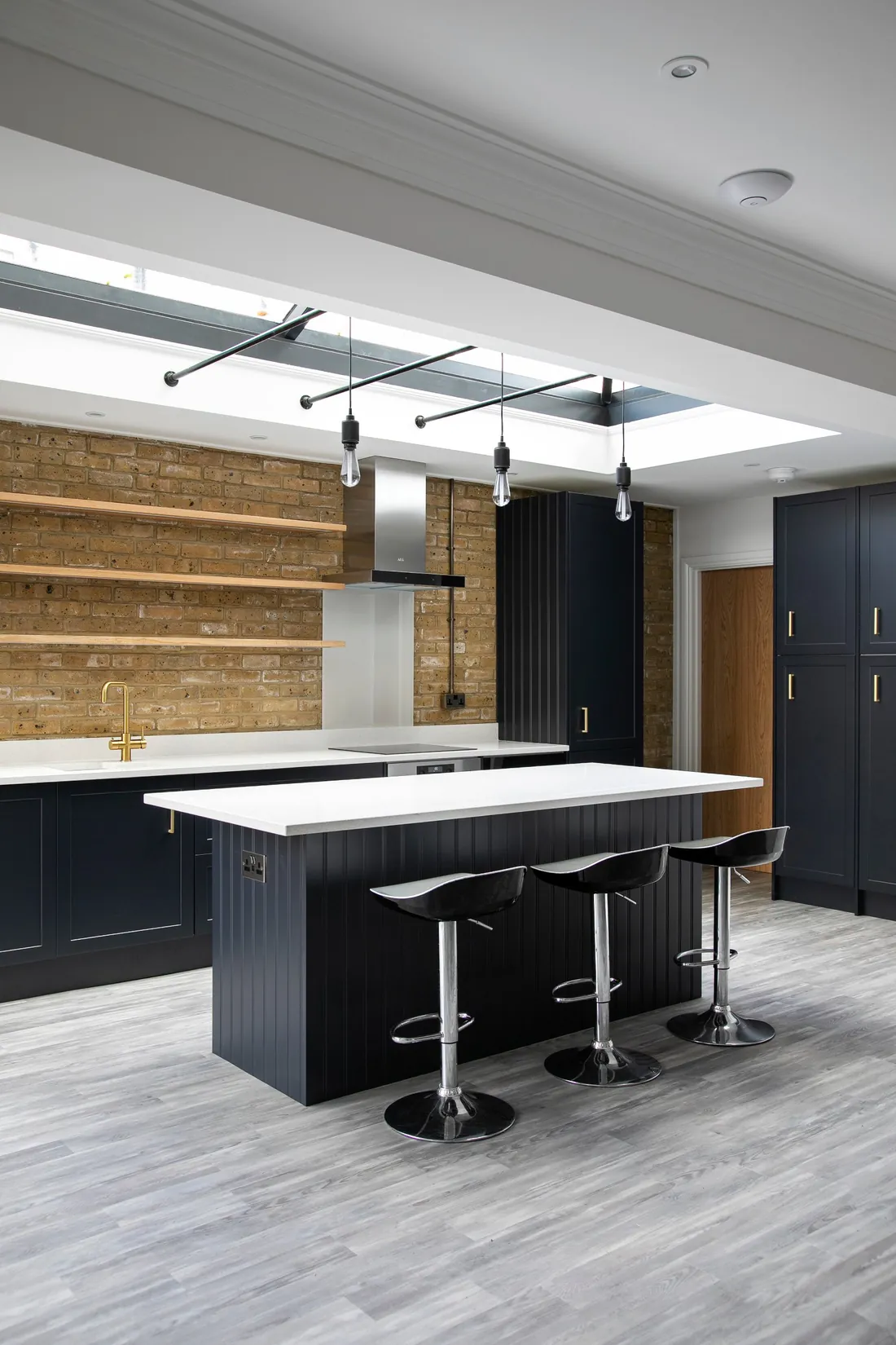 Panelled navy kitchen island with a white worktop and three bar stools under pendant lights