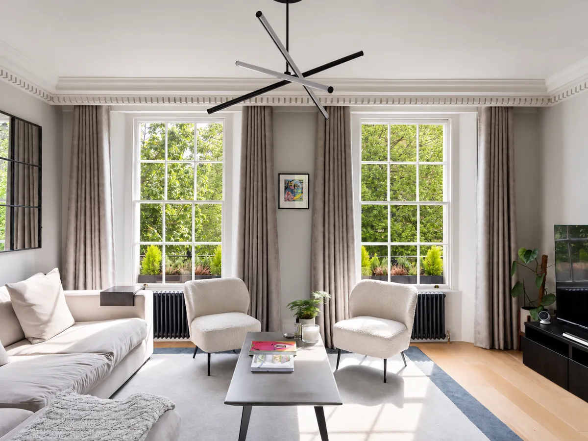 Living room in a Chelsea period home with two tall sash windows, full-height curtains and dentil cornicing